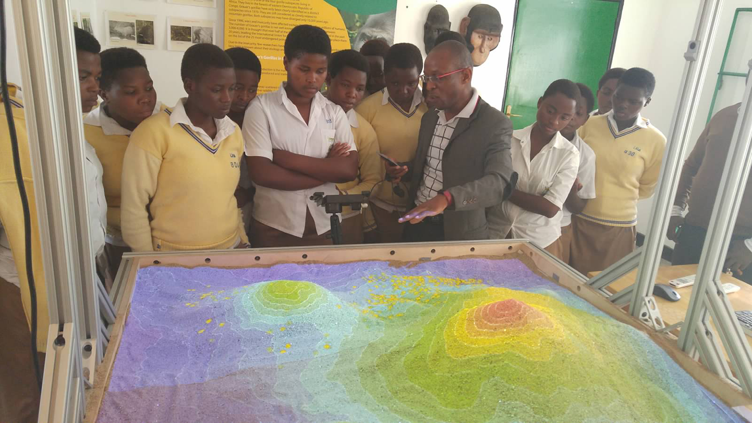interactive sandbox with school children standing around it. 