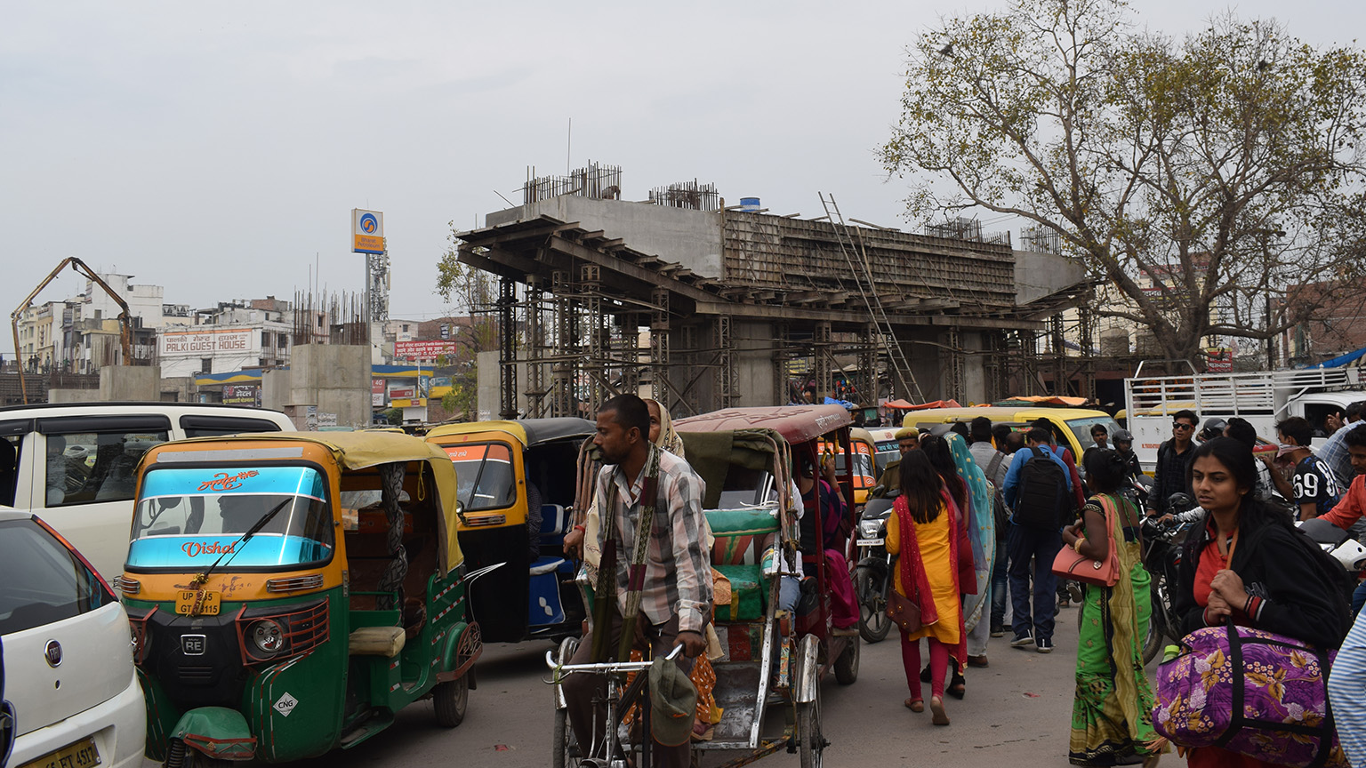 The area outside the transit station bustles with pedestrians. Construction for an overhead bridge is underway.